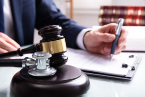 Stethoscope next to a gavel on a table where a business person writes legislation.