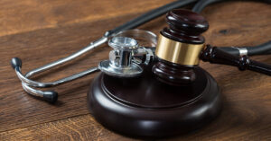 A wooden gavel and silver metal stethoscope laying atop a wooden table