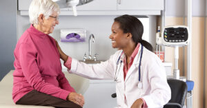 A female doctor sitting in a chair beside an smiling elderly female patient