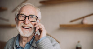 Senior man with black glasses is laughing and talking on his cell phone