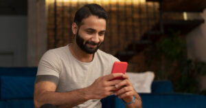 A man sitting in his living room and smiling while using his cell phone