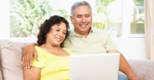 A smiling senior couple sitting on a couch in their home using a laptop