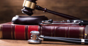 A gavel sits atop a leather book on a wooden table with a stethoscope next to the book