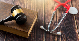 Atop a dark wooden table is a brown book , a judge's gavel, and a red stethoscope