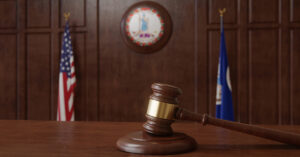 A wooden gavel in a courtroom with the American flag and Virginia state flag behind it