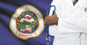 A doctor with a white coat and blue stethoscope stands in front of the Minnesota state flag