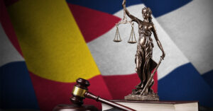 A metal statue of Lady Justice and a wooden gavel with the Colorado state flag waving behind them