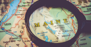 A magnifying glass focuses on Maine state on a map.