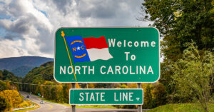 A road sign that says "Welcome To North Carolina State Line" with a landscape behind it