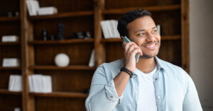 A smiling man gazes out the window of his house while talking on the phone