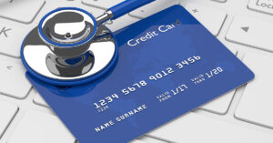 A blue credit card and a blue and silver stethoscope sit atop a white computer keyboard