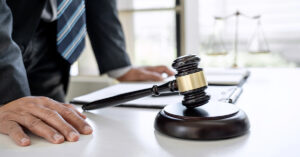 A man wearing a striped tie leans on his desk with papers and a gavel