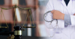 A doctor is holding a stethoscope and standing next to the scale of justice and a gavel