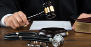 A hand holding a gavel with a stethoscope laying on the table next to it