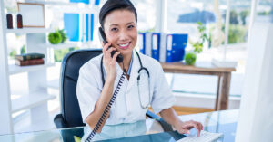 A healthcare professional is smiling at her desk and talking on the phone