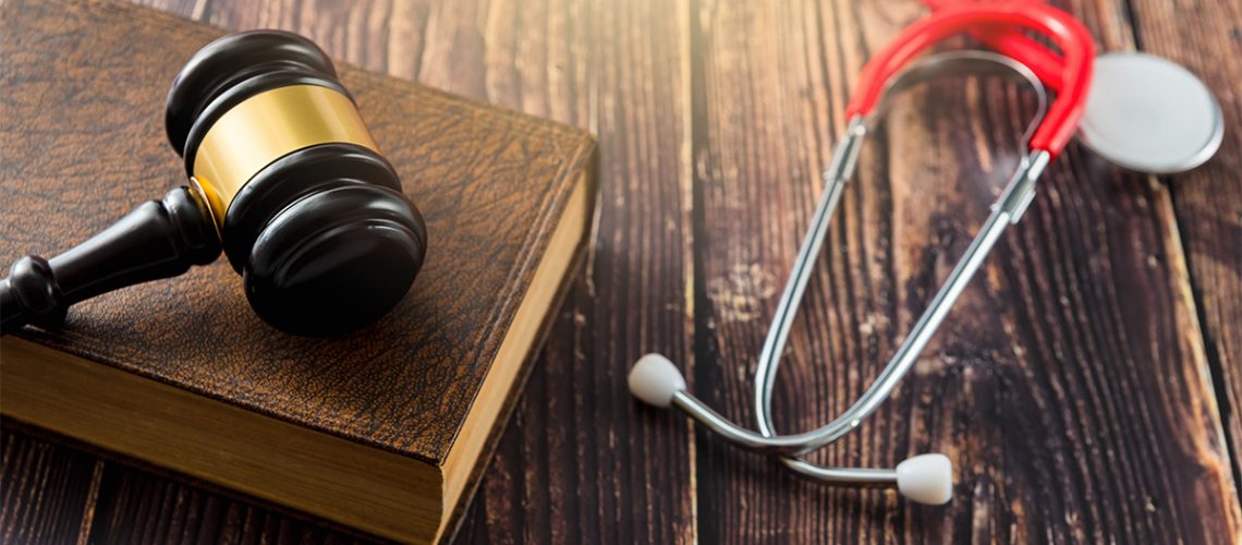 Atop a dark wooden table is a brown book , a judge's gavel, and a red stethoscope