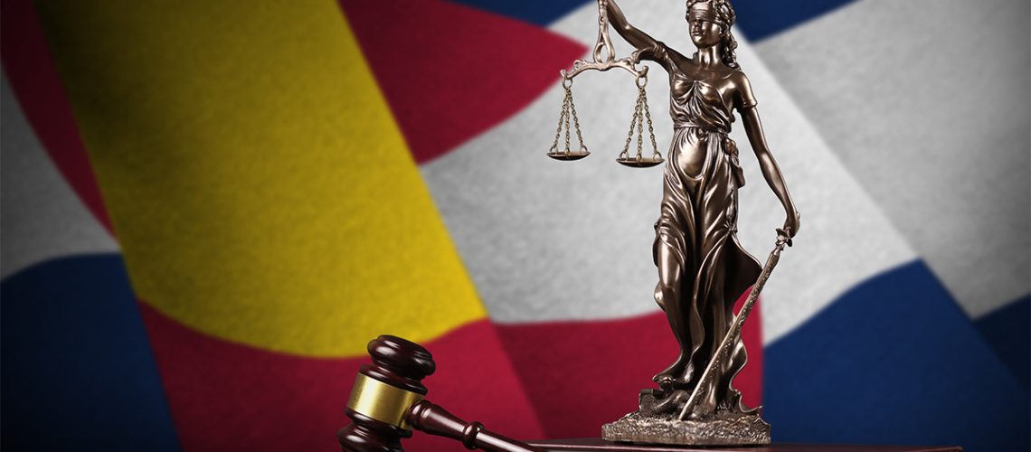 A metal statue of Lady Justice and a wooden gavel with the Colorado state flag waving behind them