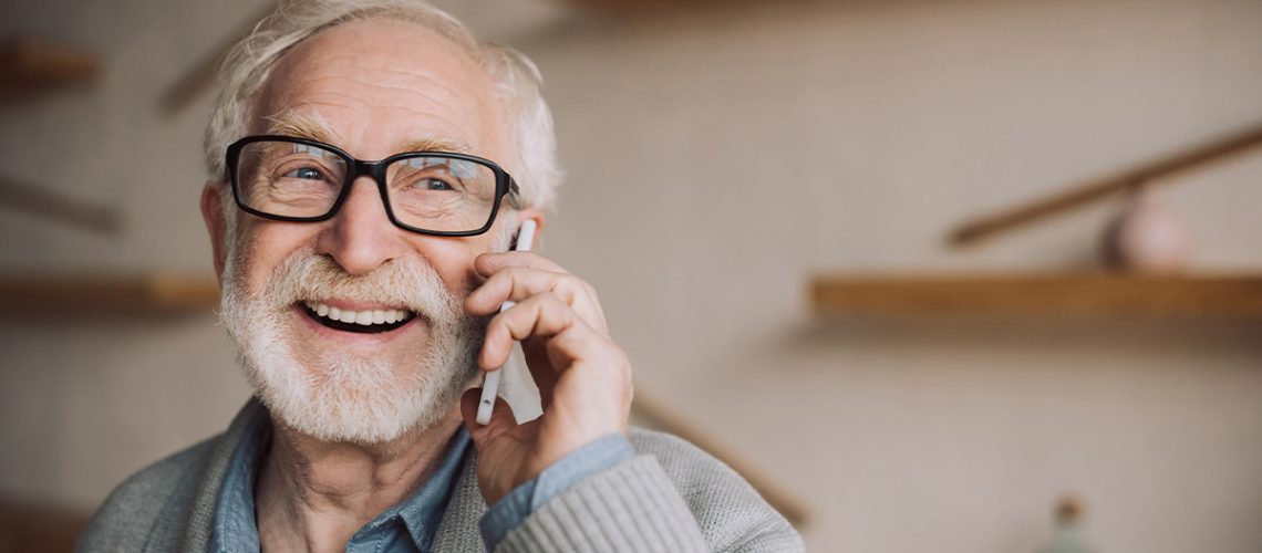 Senior man with black glasses is laughing and talking on his cell phone