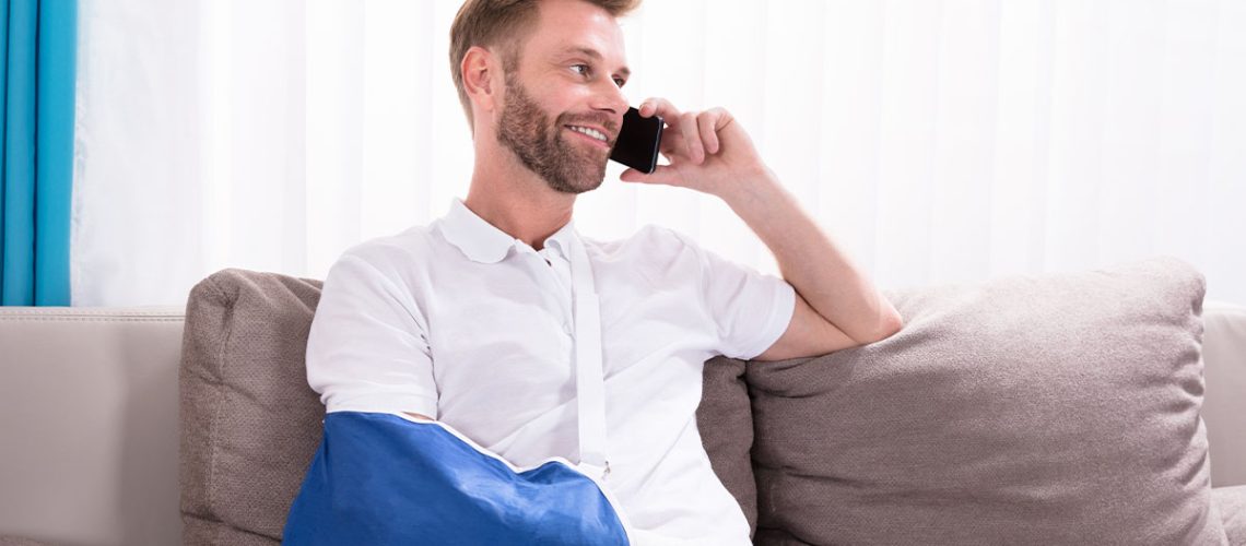 Man sitting on a couch with a blue sling and talking on the phone