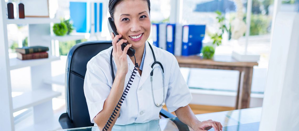 A healthcare professional is smiling at her desk and talking on the phone