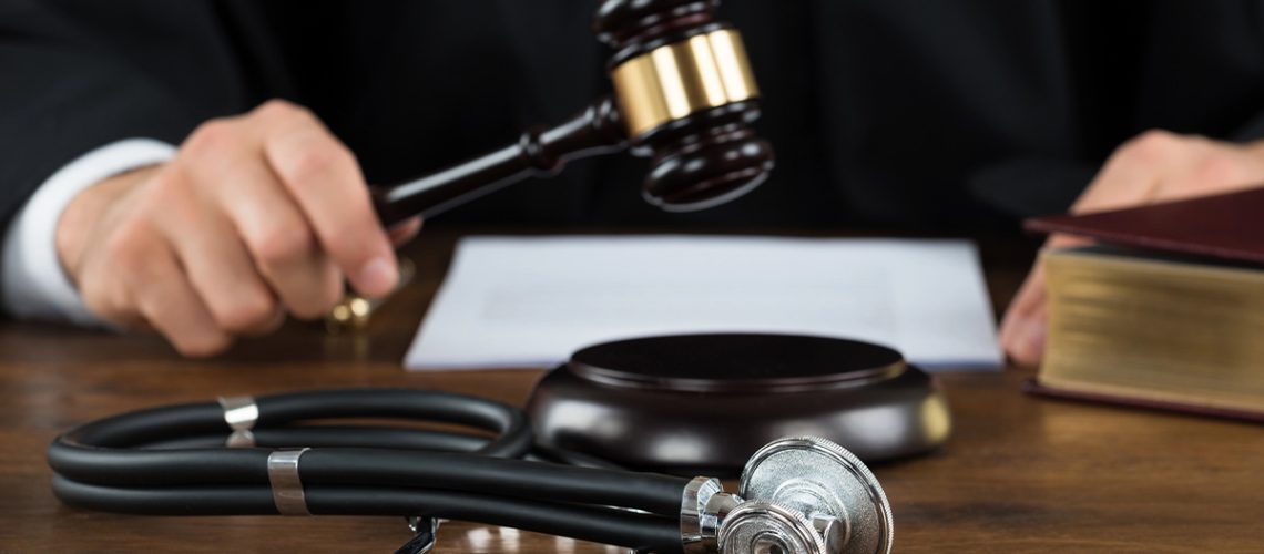 A hand holding a gavel with a stethoscope laying on the table next to it