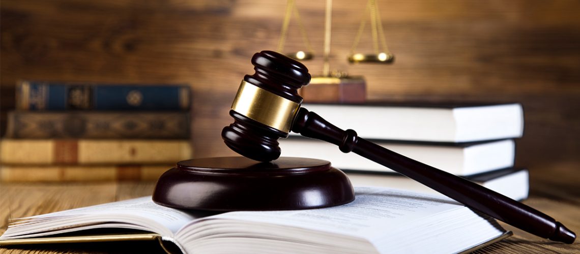 Wooden gavel atop an open hardcover book with a stack of 3 books behind it