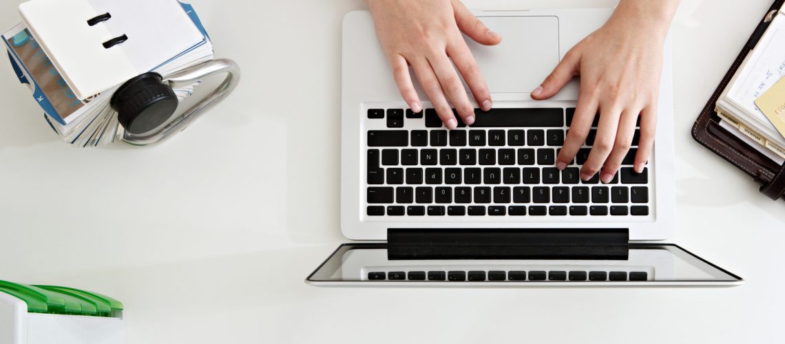 A laptop on a desk with a person's hands typing on the keyboard.