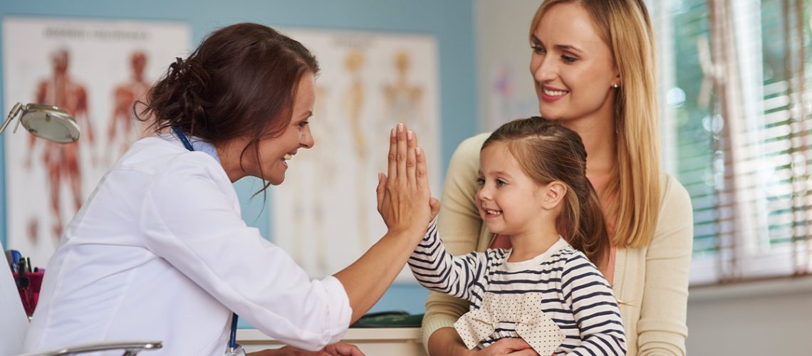 A child sitting in her mothers lap, high fiving her doctor in the doctors office