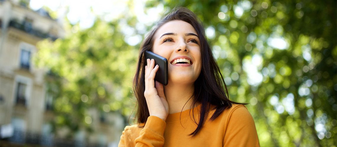 A woman smiles while talking on her cell phone outdoors