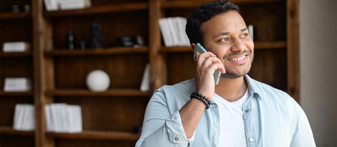 A smiling man gazes out the window of his house while talking on the phone