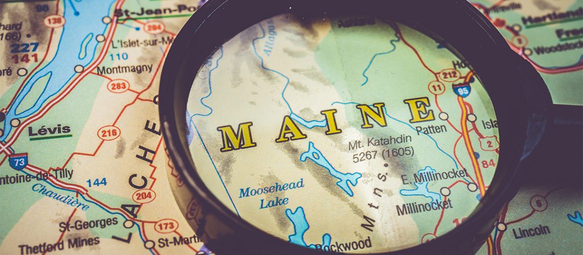 A magnifying glass focuses on Maine state on a map.