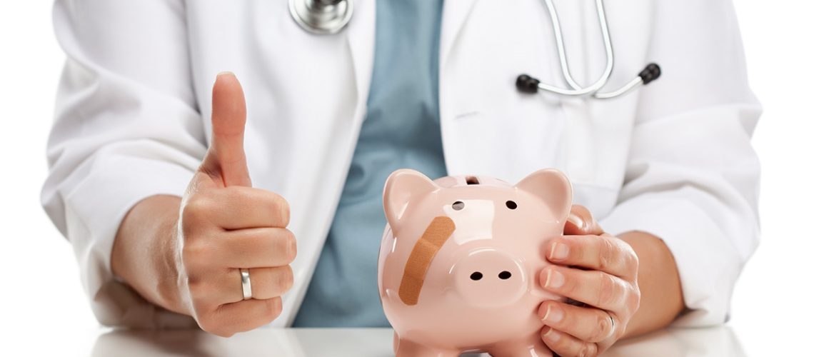 A doctor with a stethoscope around their neck is gesturing a thumbs-up with one hand and their other hand is resting on a pink piggy bank that has a band aid on it