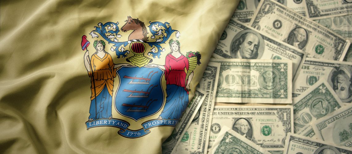 The New Jersey State flag is laying atop scattered $1- and $10- and 100-dollar bills