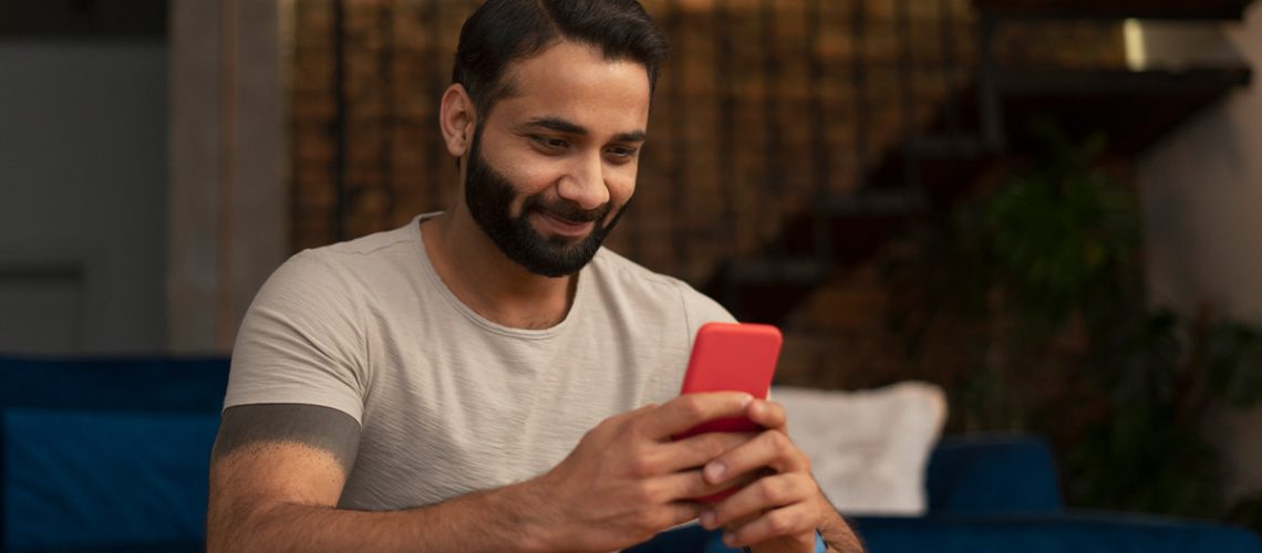 A man sitting in his living room and smiling while using his cell phone