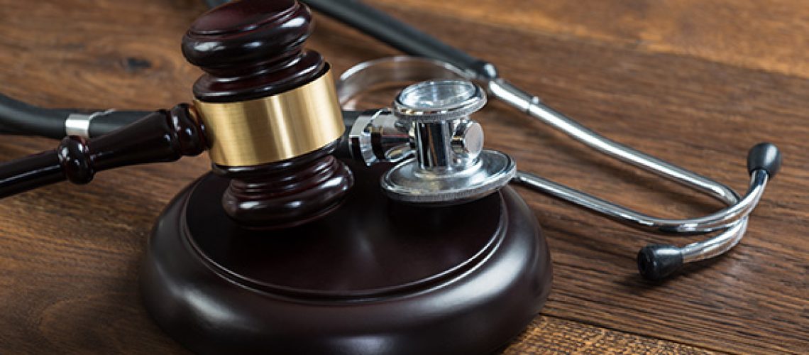 A wooden gavel and a black and silver metal stethoscope sit atop a wooden table