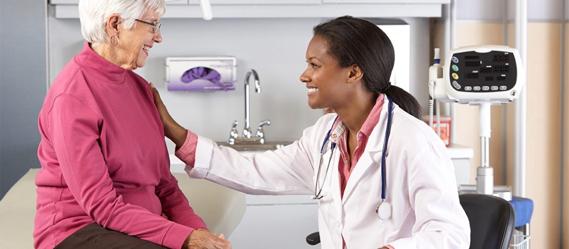 A female doctor sitting in a chair beside an smiling elderly female patient