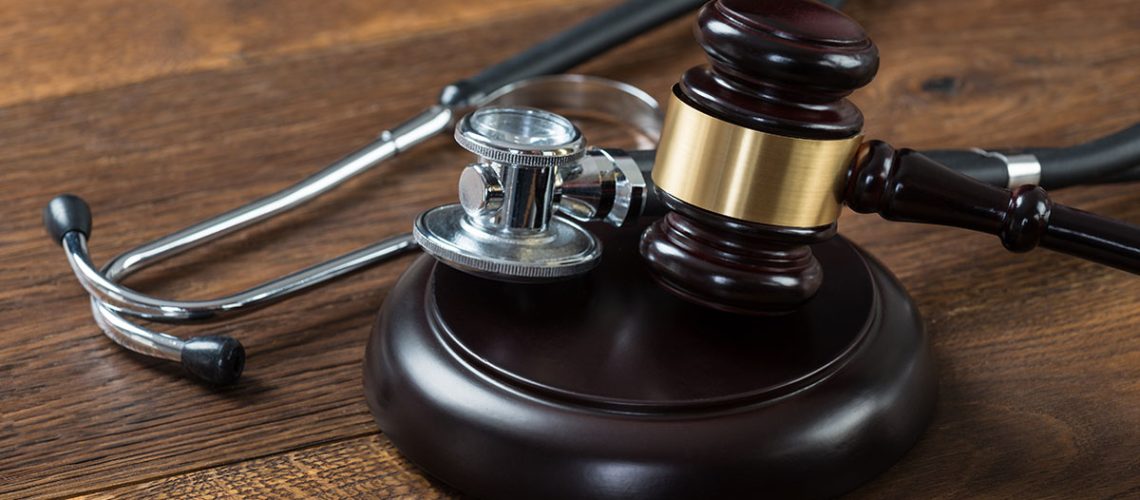 A wooden gavel and silver metal stethoscope laying atop a wooden table