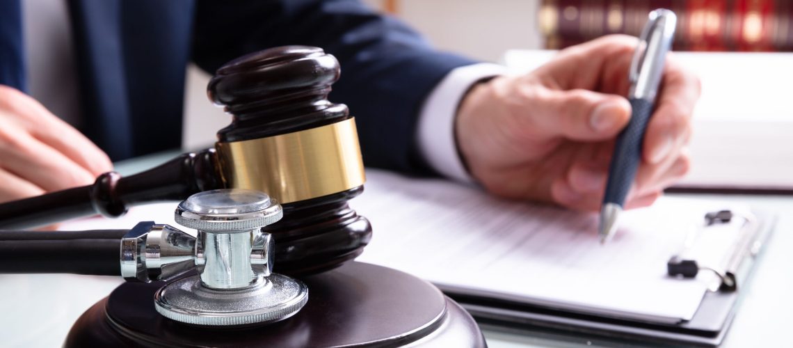 Stethoscope next to a gavel on a table where a business person writes legislation.