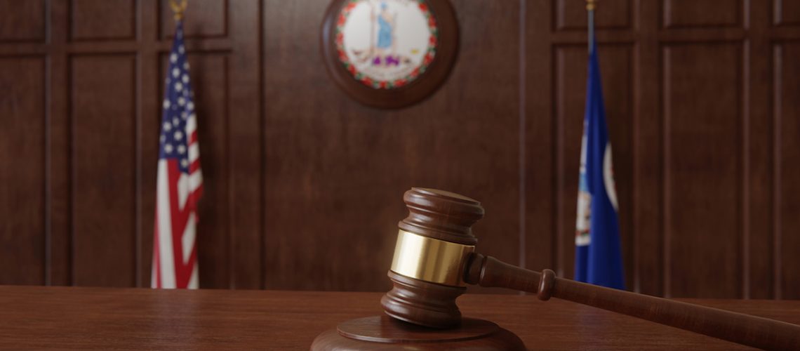 A wooden gavel in a courtroom with the American flag and Virginia state flag behind it