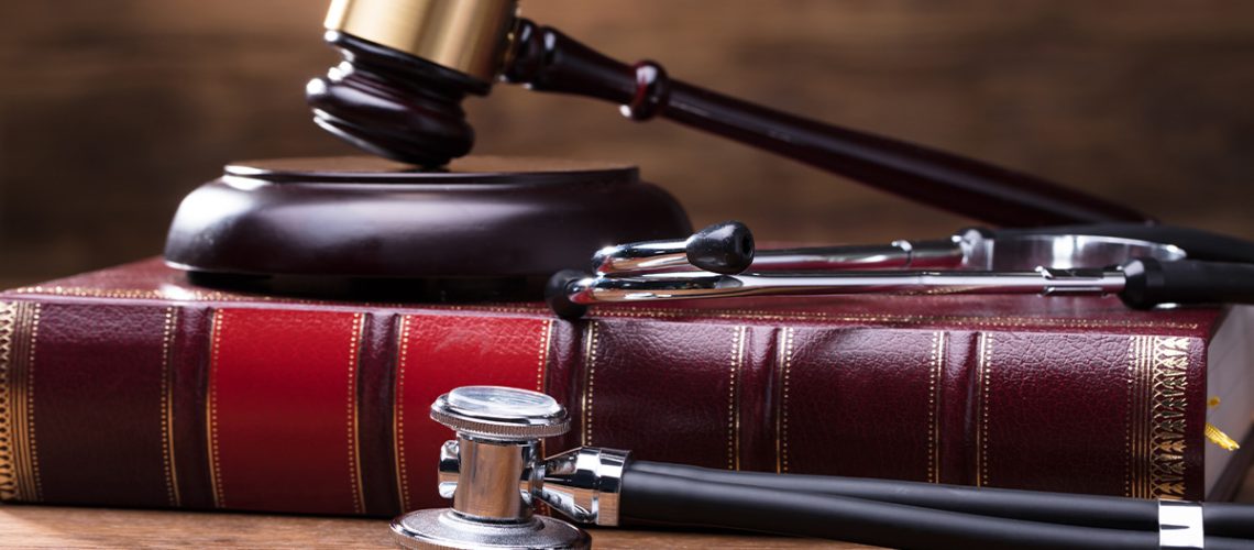 A gavel sits atop a leather book on a wooden table with a stethoscope next to the book