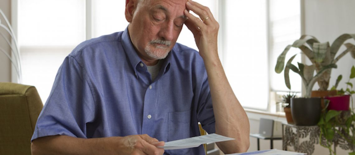 Older man looking frustrated while reviewing bills